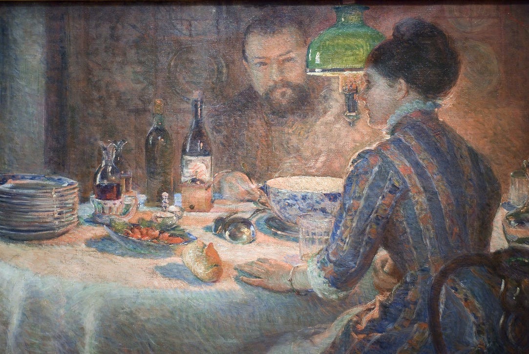 Marie Bracquemond Under The Lamp (1887) depicts a rich dinner scene under a gas lamp. There’s a white table cloth, bottles of wine, a stack of plates and bread. There is a large steaming bowl of soup between a man and a woman. We see the profile of the woman and her back, her braceleted hand is on the table and she looks like she’s in the middle of saying something. The man across the table is looking at her as she speaks.