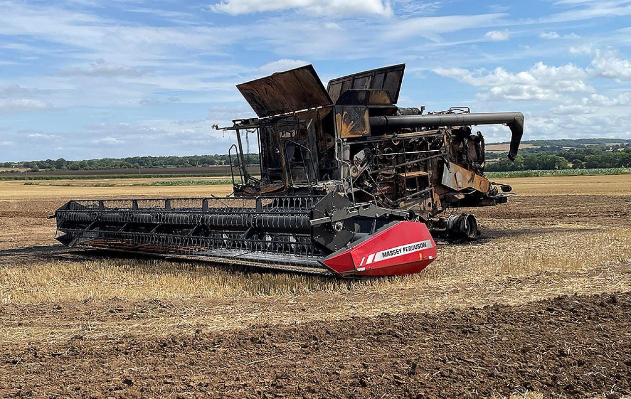 A soot stained burnt-out harvester sits in a recently harvested field.