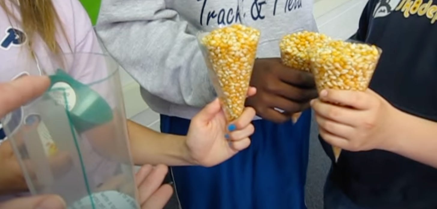 An image of kids holding three cones of full of corn kernels next to a cylinder.