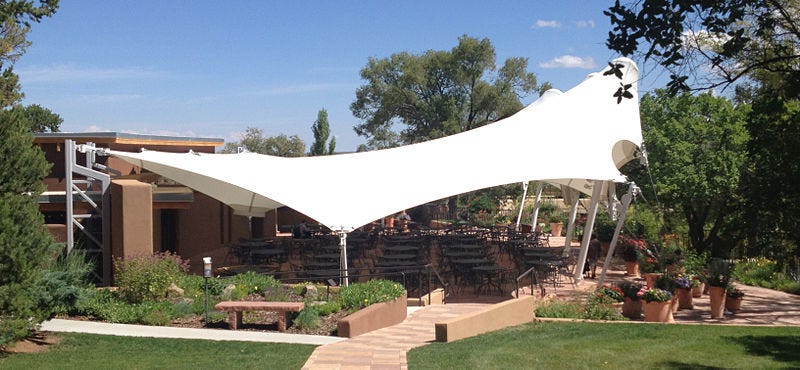 Photo of a covered pavilion over outdoor seating in a garden setting.