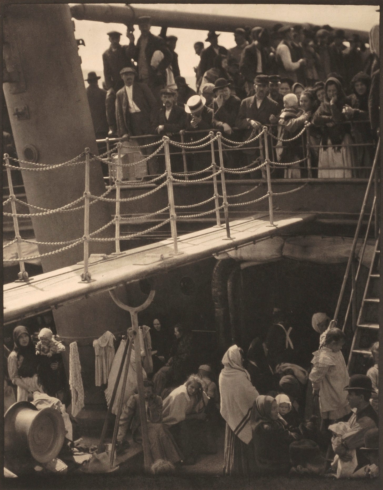 Black and white photo of people crowded on the decks of a ship and lines of clothes drying.