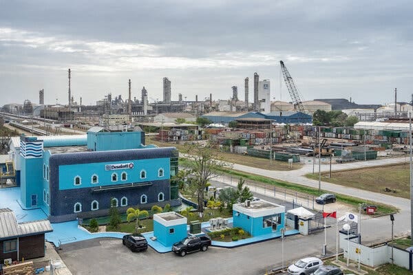 A blue-colored desalination plant is in the foreground and there are industrial facilities in the background.