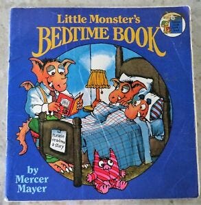 Two cartoon creatures lay in a bed with pillow and blankets, while a third, older, cartoon creature reads them a story. A striped pink stuffed monster toy sits on the floor next to the bed.