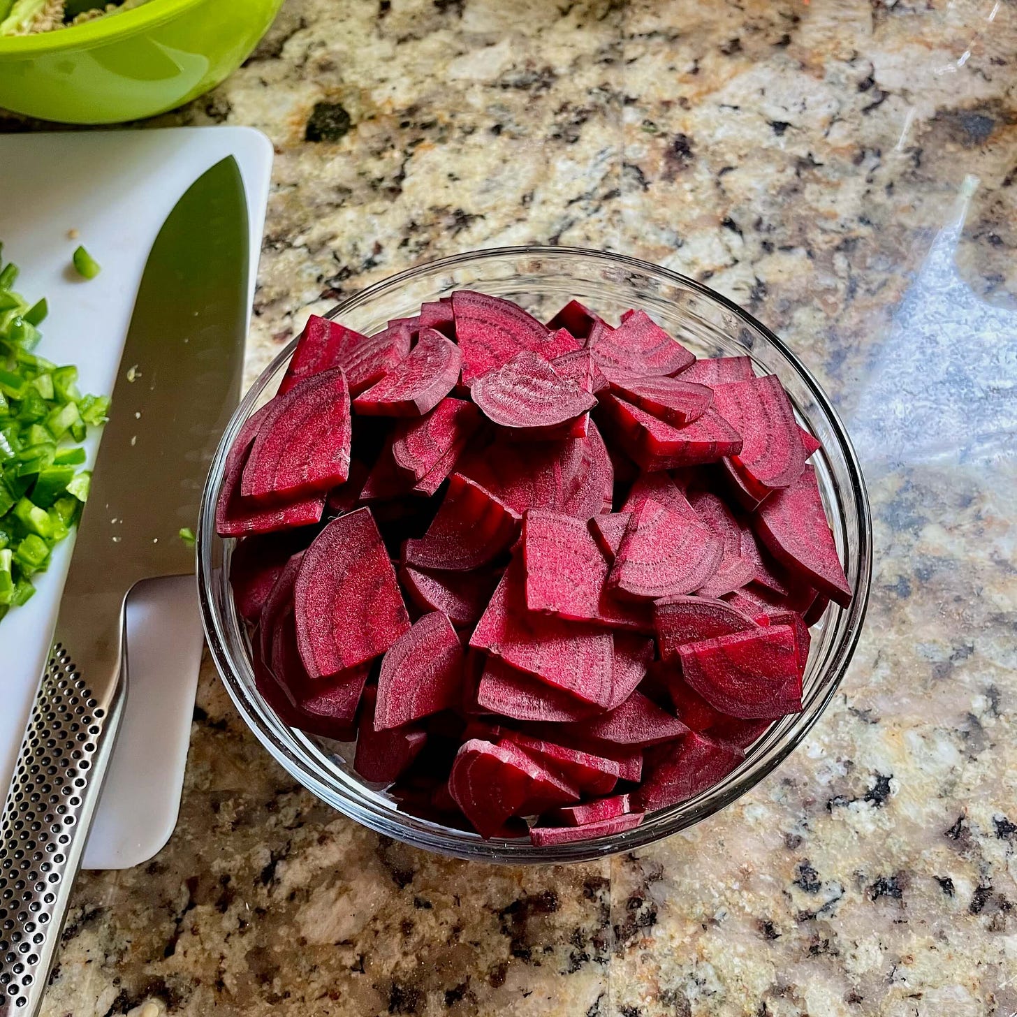 A bowl of quartered and thinly sliced beets, with a knife to the side.