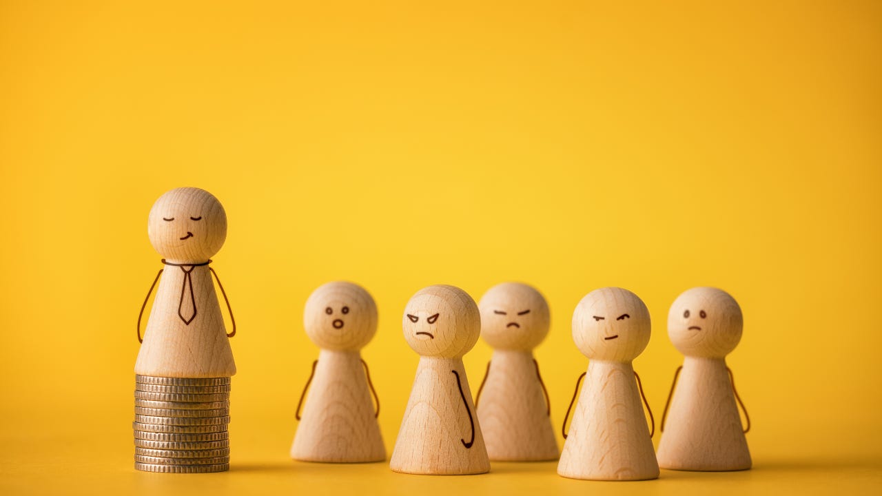 Wooden figures standing by a wooden figure on a stack of coins.