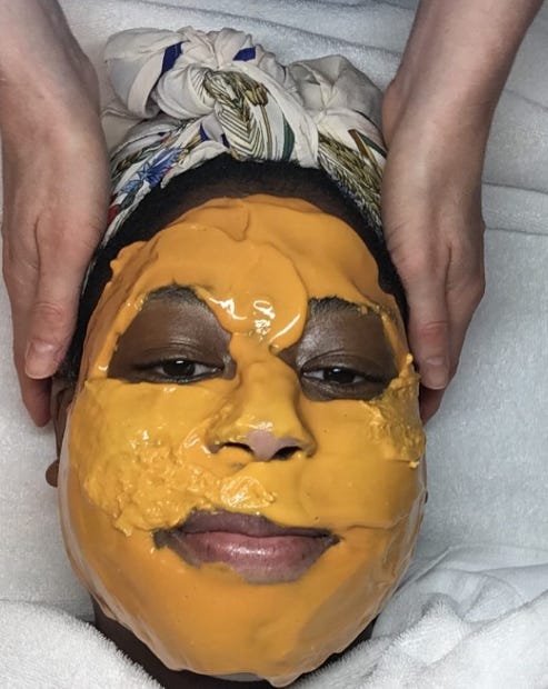 A portrait of Chanel with a yellow-orange skin care mask on her face during a facial. 