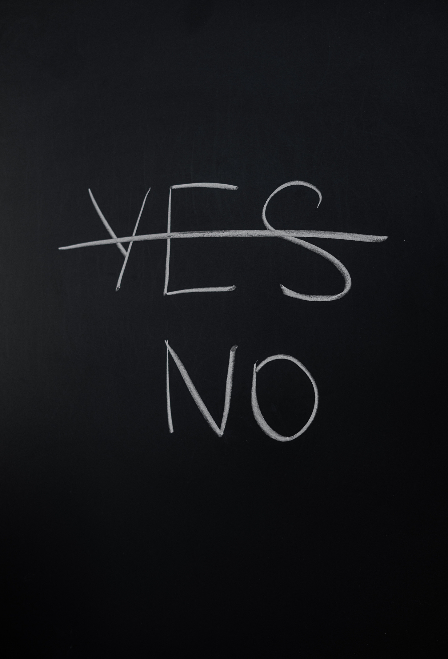 the words yes and no appear in white chalk on a blackboard, however the word yes is crossed out