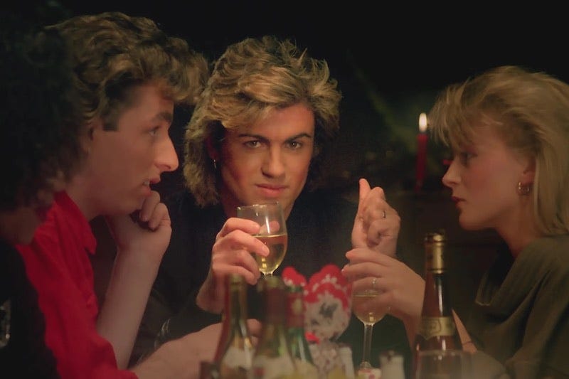 Still from Last Christmas video where George Michael holds a glass of wine and looks into the camera as if gazing at someone across the room