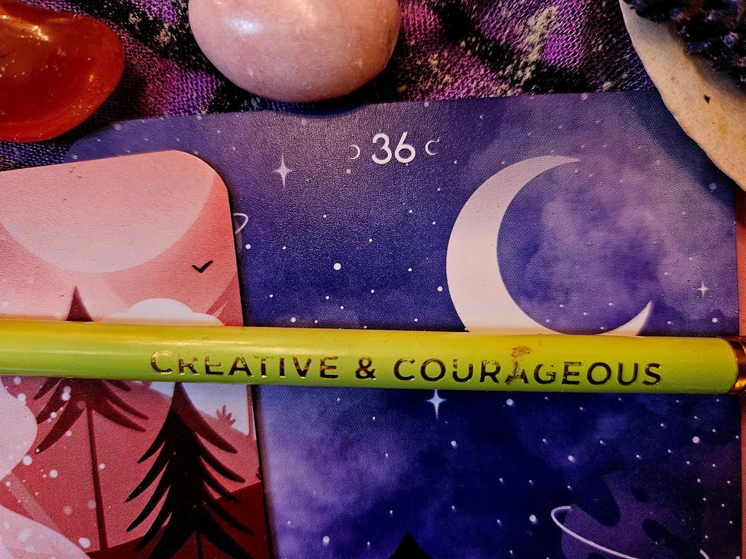 The yellow green “creative and courageous” pencil from my writing session in Emily Dickinson’s bedroom (Real Writing in the World #9) on a background of orange and purple oracle cards showing trees and a moon, and orange-red carnelian and pink Mangano calcite crystals.