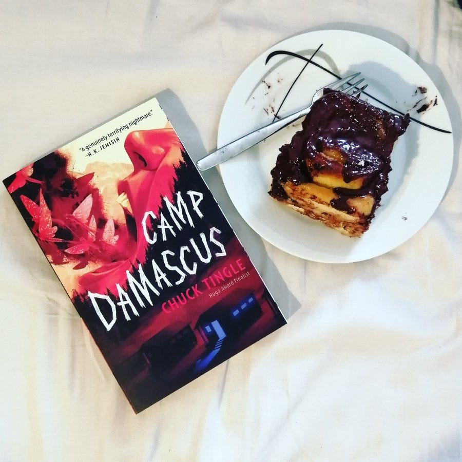 Das Buch "Camp Damascus" von Chuck Tingle neben einem Teller mit einer Schokoladenschnecke