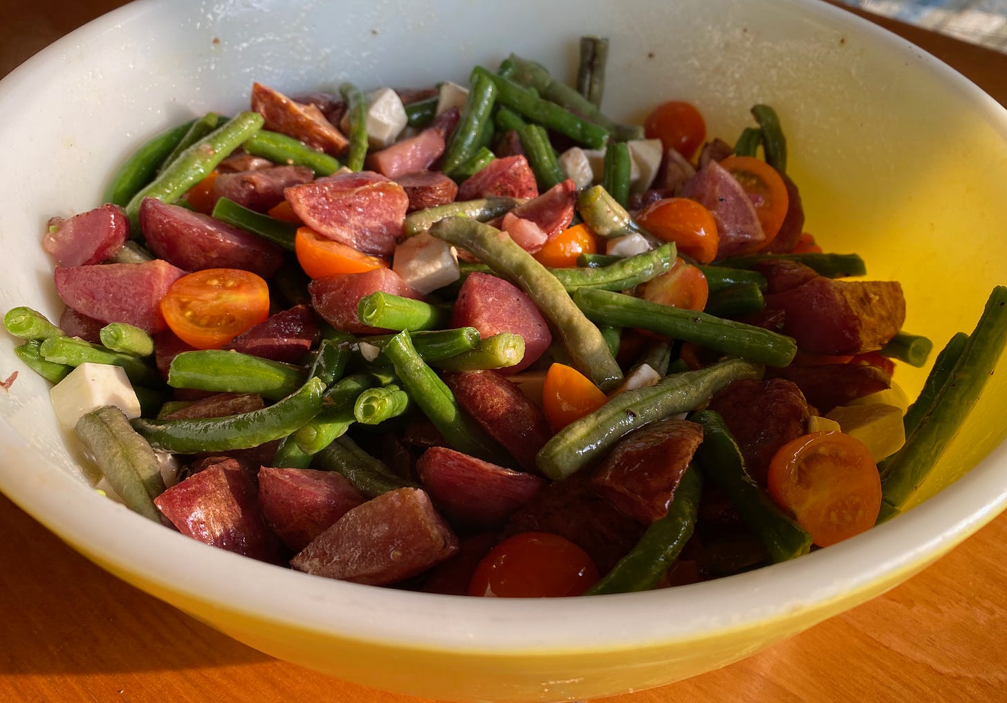 A large bowl of roasted red potatoes, green beans, sungold tomatoes, and chunks of fresh mozzarella. 
