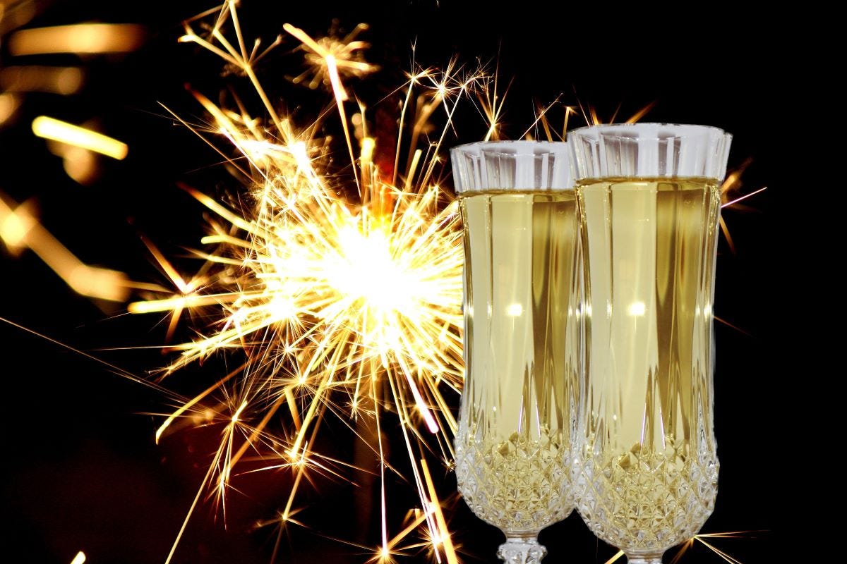 Two filled champagne flutes with a sparkler in the background