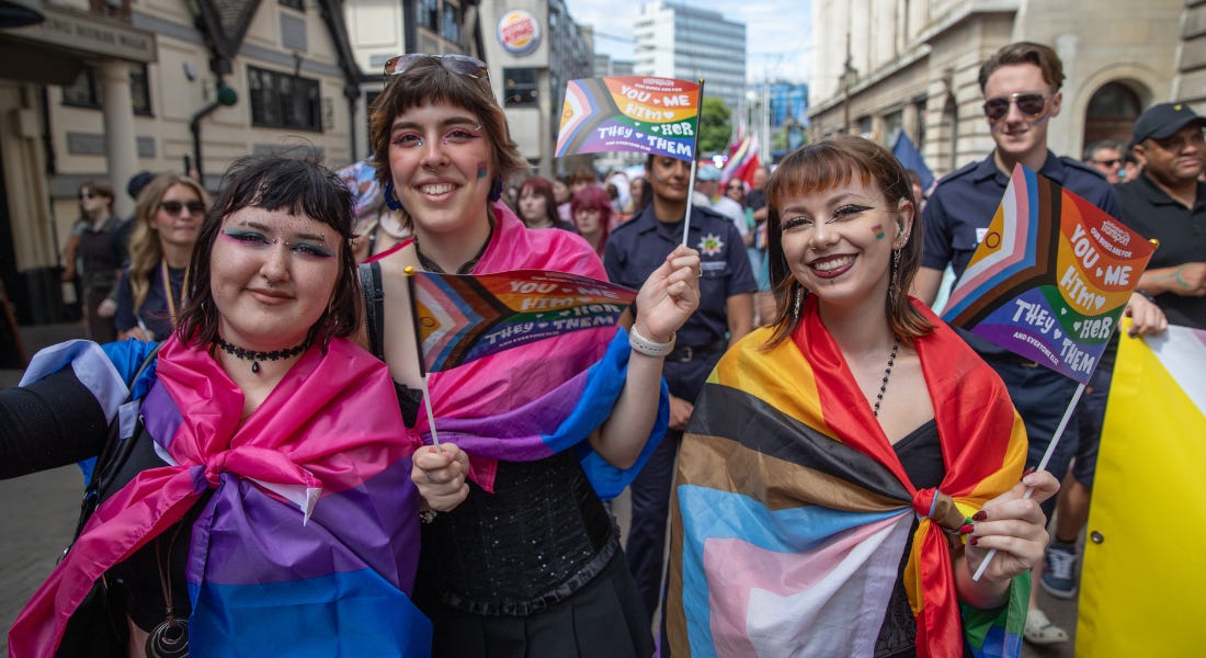 Three people wearing flags smiling in the camera, with a crowd of people behind them