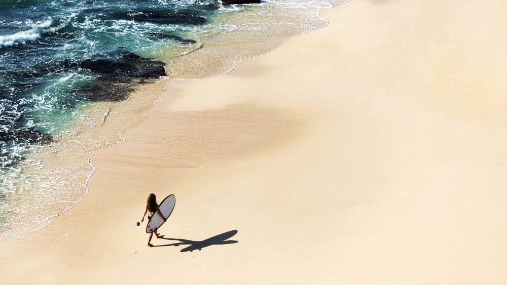 Girl with surfboard walks on beautiful beach.