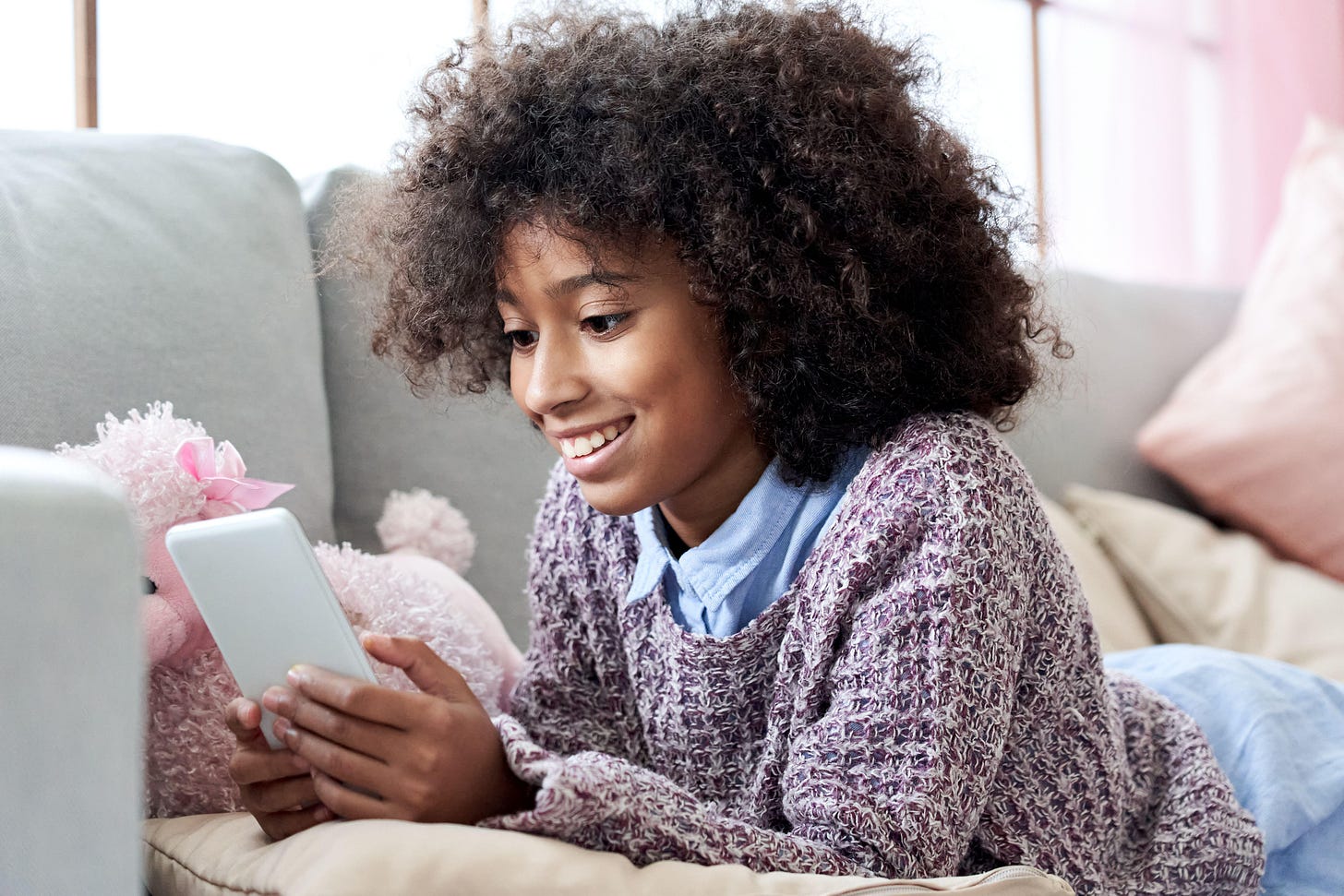 Happy african child girl using mobile apps on phone relaxing on couch at home.