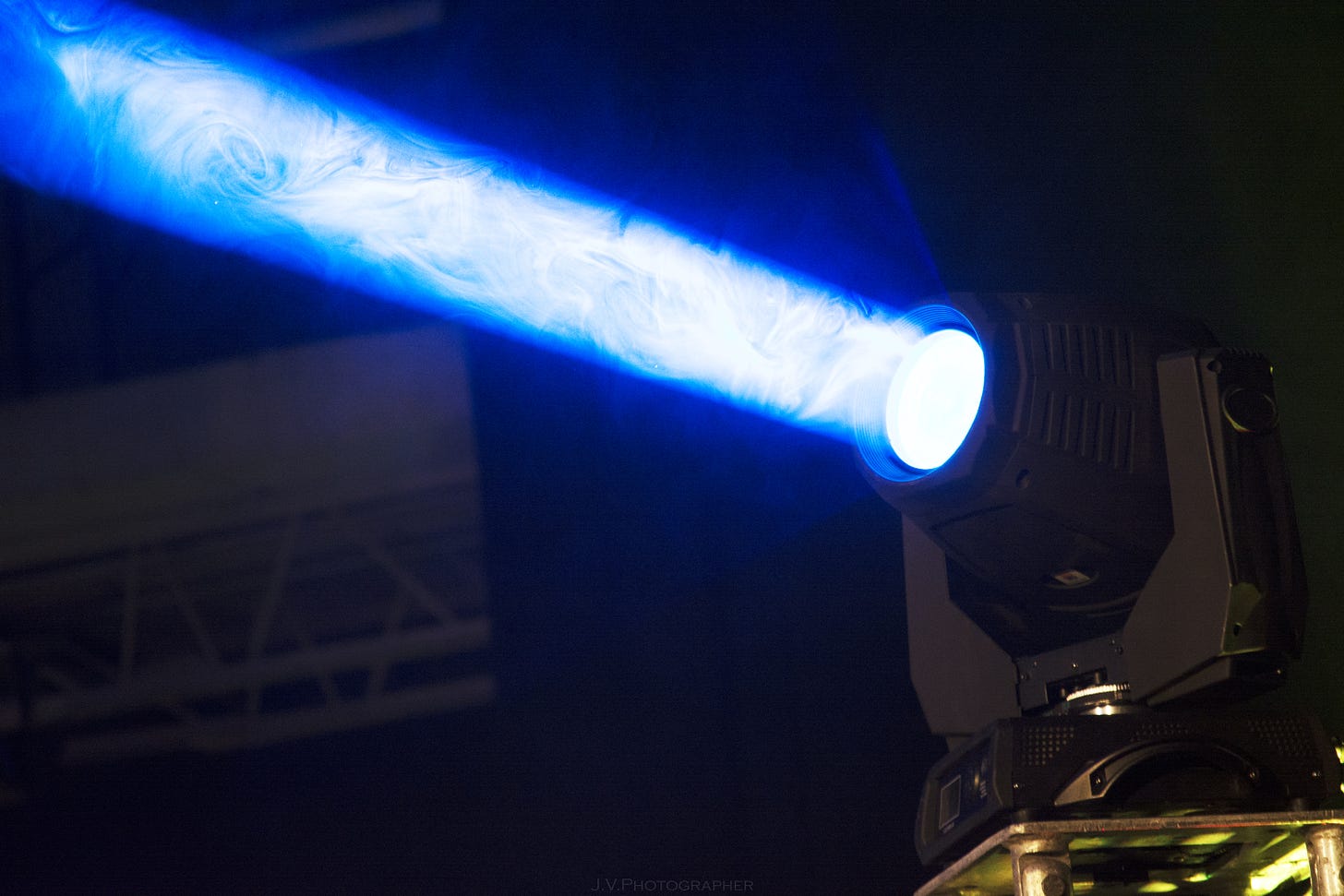 A spotlight machine projects a blue beam of light into a dark room.