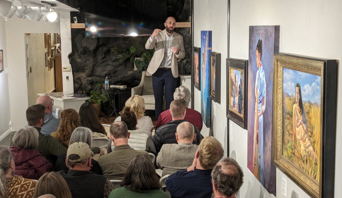 Man in an art gallery speaking to an audience.