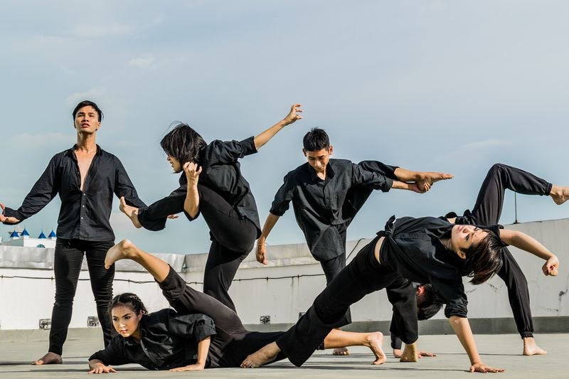 Six people, all wearing matching black clothes, artistically arranged in different flexible poses