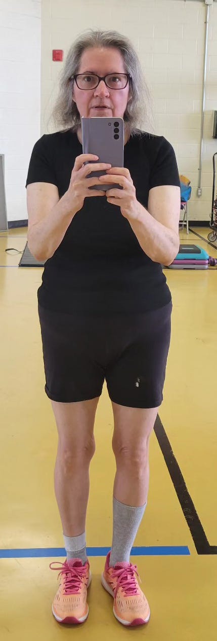 Woman in gym in front of a mirror in workout clothes, holding her phone