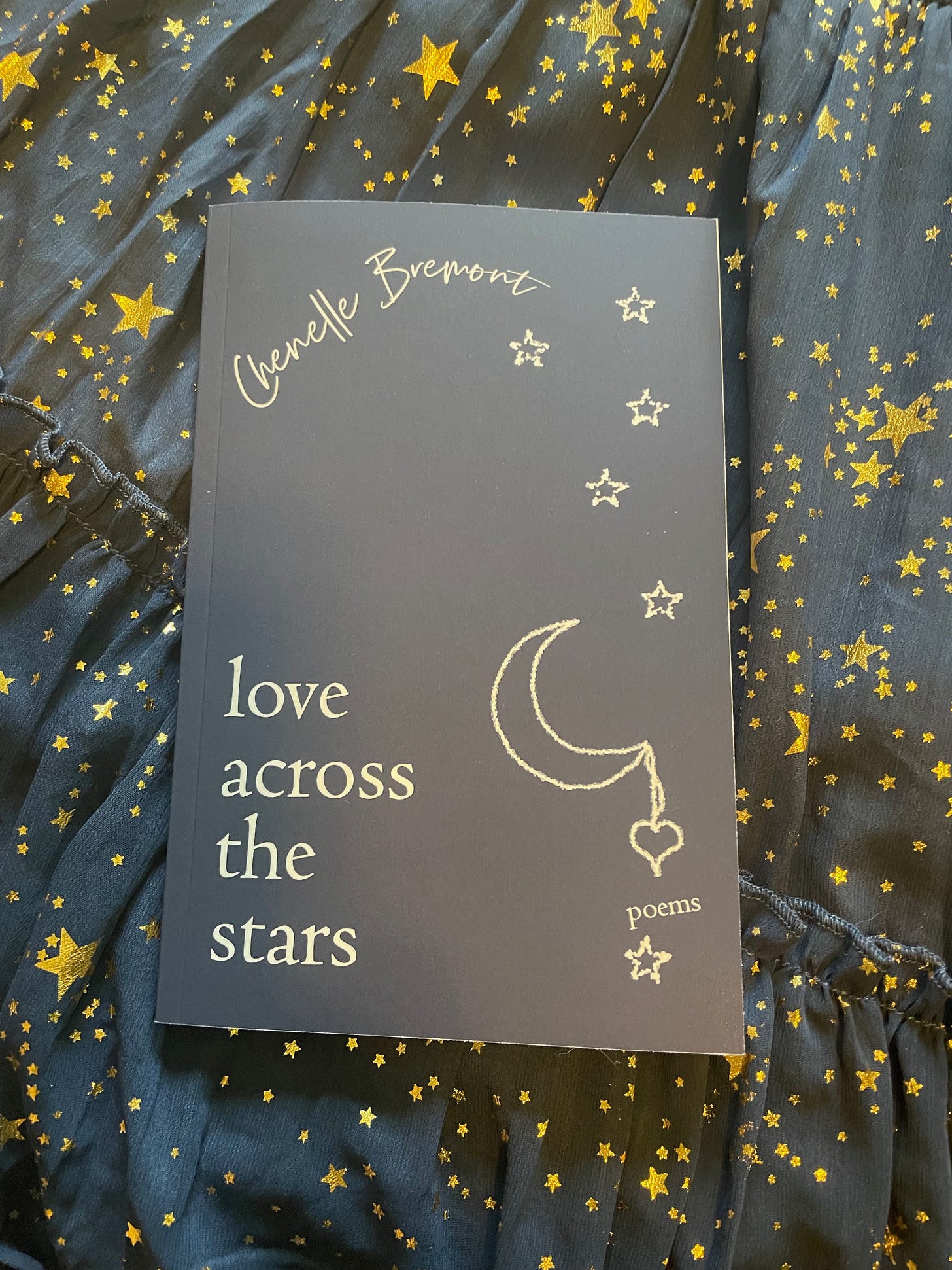 Chenelle's book, navy blue with chalk drawings of a crescent moon and stars, on crinkly blue fabric with gold stars.