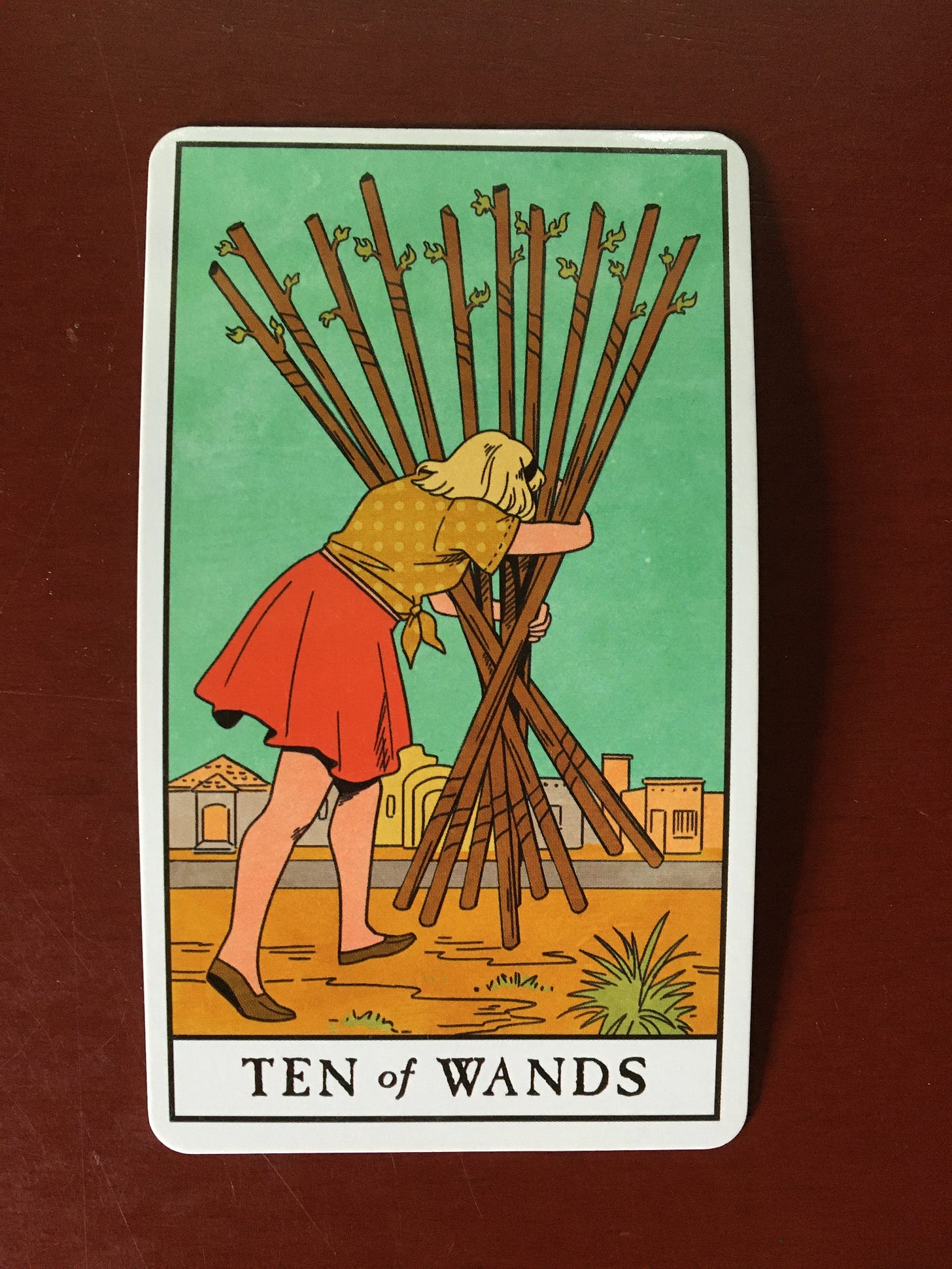 Ten of Wands card that shows a person holding a bundle of (ten) sticks/ wands, which blocks what's ahead