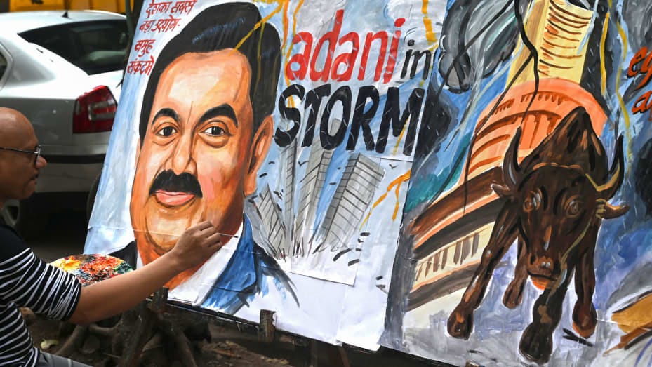 Art school teacher Sagar Kambli gives final touches to a painting of Indian businessman Gautam Adani (L) highlighting the ongoing crisis of the Adani group in Mumbai on February 3, 2023.