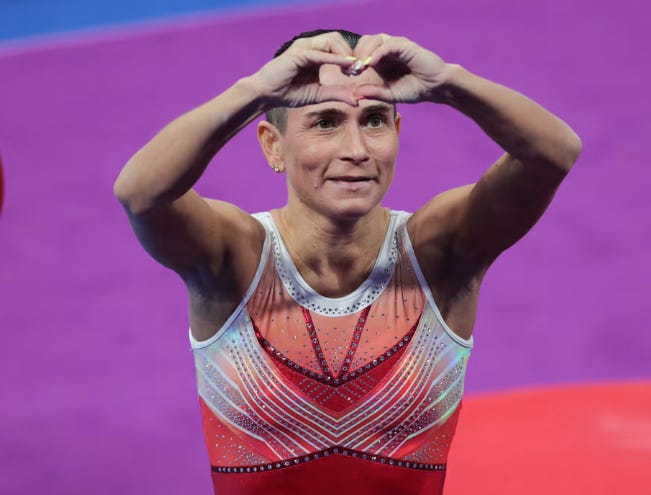 A person in a leotard making a heart with her hands

Description automatically generated