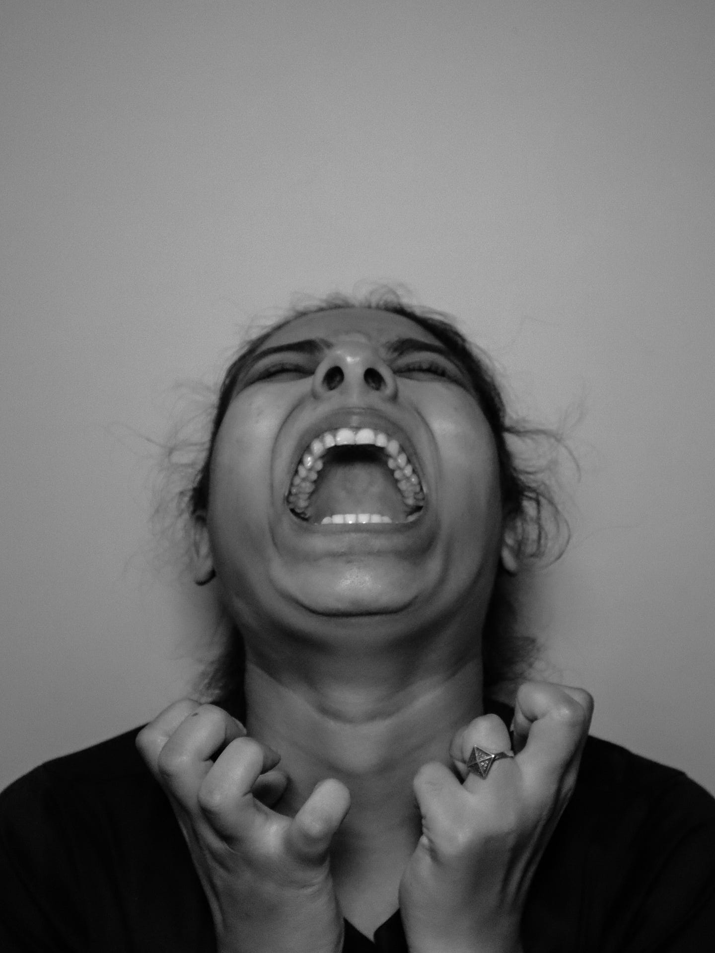 Woman of colour has her hands curled in frustration, near her face that is thrown back. Her mouth is open and eyes are tightly closed. It looks like she’s yelling in frustration. Woman of colour has her hands curled in frustration, near her face that is thrown back. Her mouth is open and eyes are tightly closed. It looks like she’s yelling in frustration.