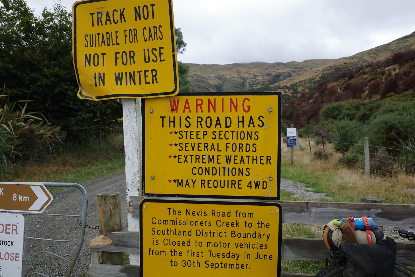 A warning sign: "This road has steep sections, several fords, extreme weather conditions, may require 4wd".