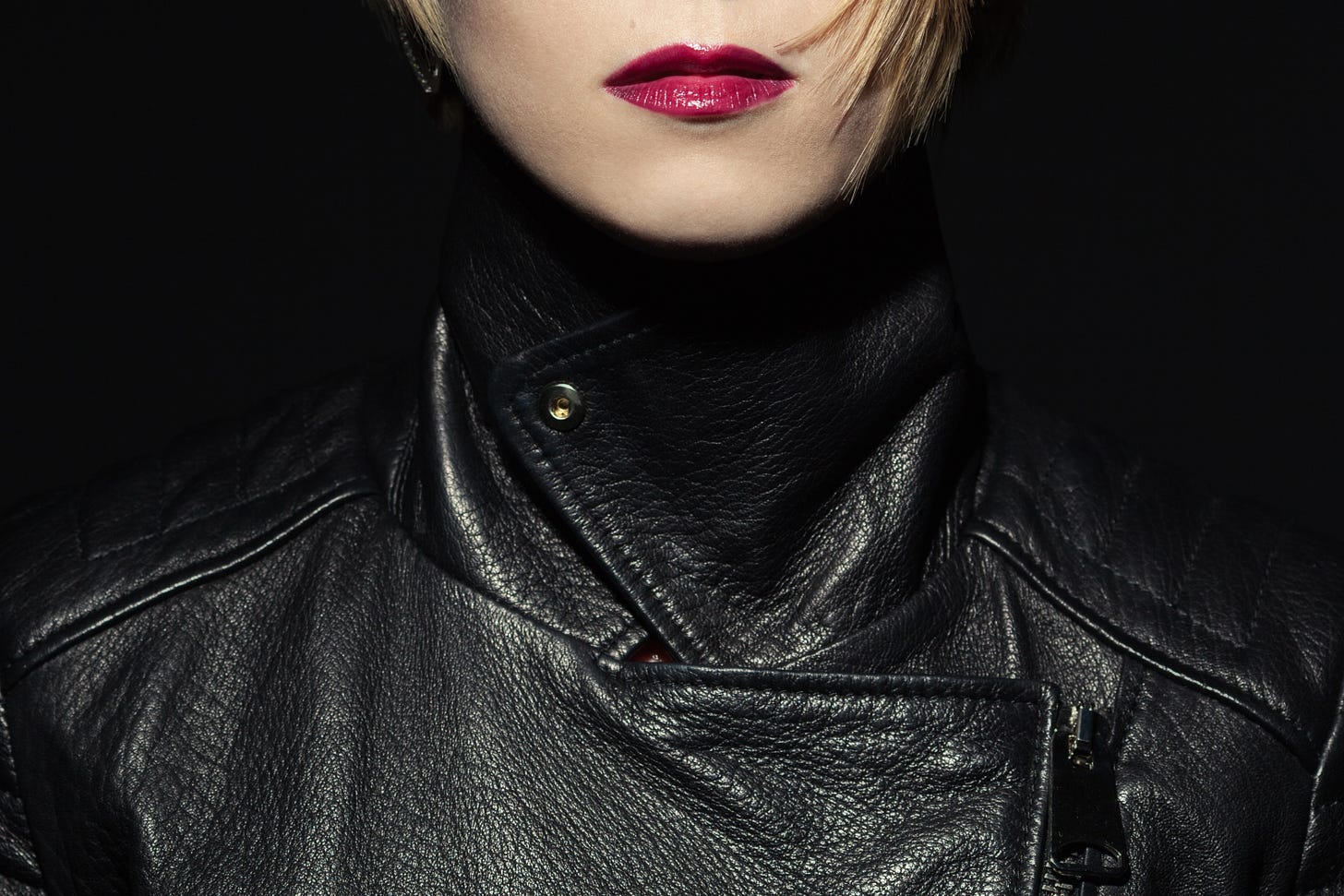 A woman in a black leather jacket and bright red lipstick, shown from the mouth down.