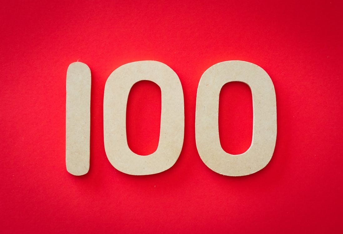 Free Close-up of numeral 100 in beige on a bright red background, emphasizing celebration. Stock Photo Free Close-up of numeral 100 in beige on a bright red background, emphasizing celebration. Stock Photo