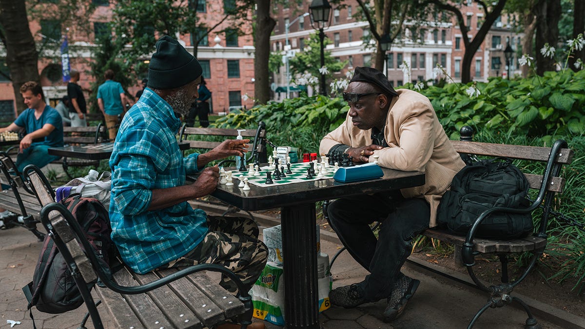 Two men playing chess at a table in a downtown urban park area