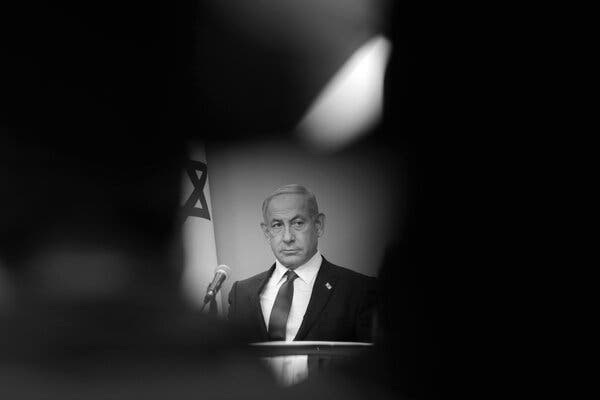 Benjamin Netanyahu at a podium in front of an Israeli flag, surrounded by darkness.