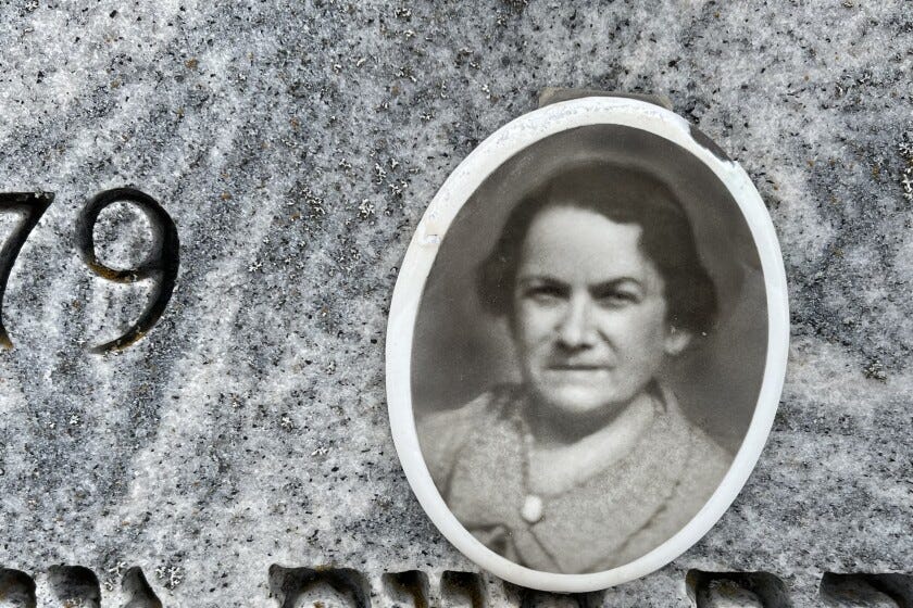 Close-up view of gravestone featuring blurry black-and-white photo of middle-aged woman. Numbers and Hebrew lettering indistinctly visible at edges of photograph.