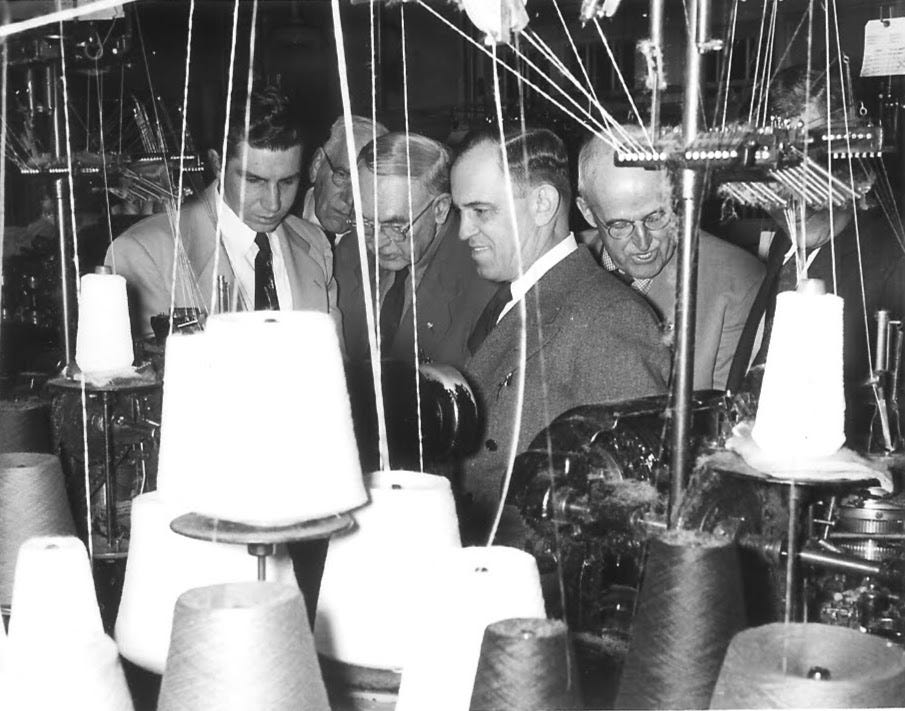 Men with ties looking at spools of thread