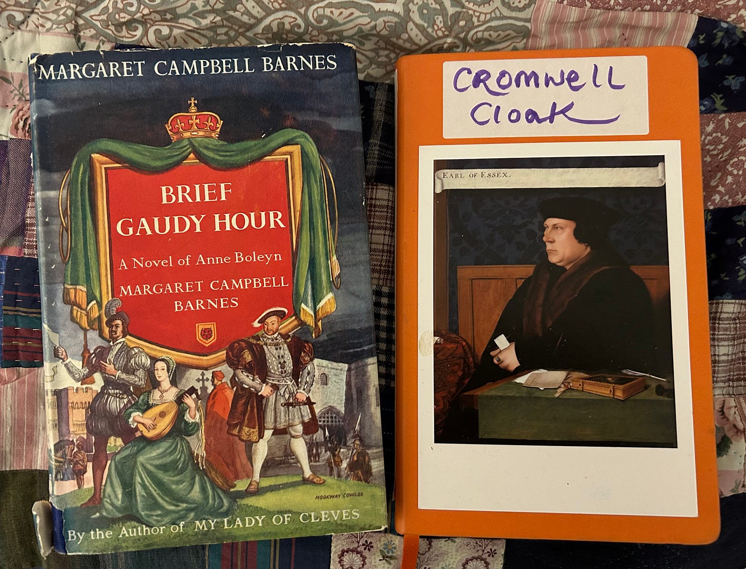 A hardback copy of Brief Gaudy Hour by Margaret Campbell Barnes, featuring pictures of Anne Boleyn playing a lute, watched by Henry VIII and Thomas Wyatt, with Cardinal Wolsey in the background. Next to this is an orange notebook, marked Cromwell Cloak, with a portrait of Cromwell stuck on the front. 