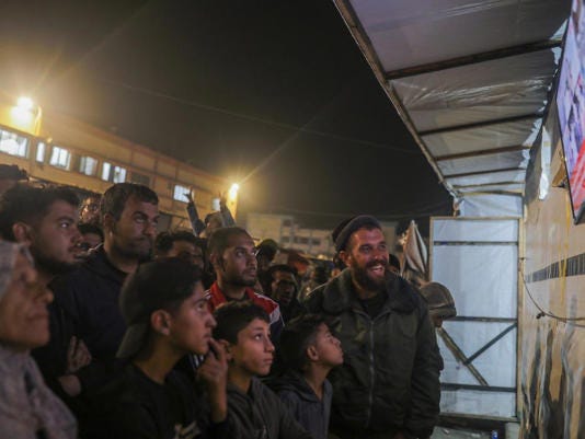 Palestinians watch television as they await the announcement of a ceasefire deal between Hamas and Israel in Khan Younis, central Gaza Strip, on Jan. 15, 2025.