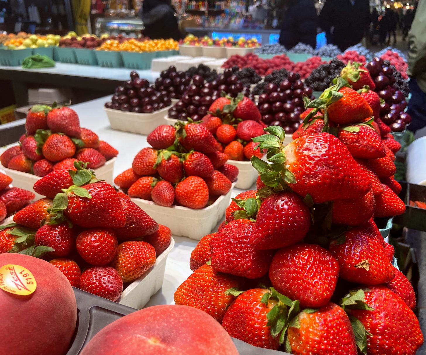 Strawberries, cherries, and other fruit piled in punnets for sale at fruit stand.