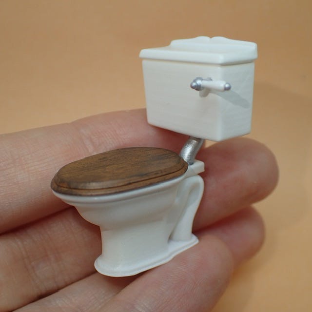 a dollhouse furniture sized toilet in the palm of someone’s hand