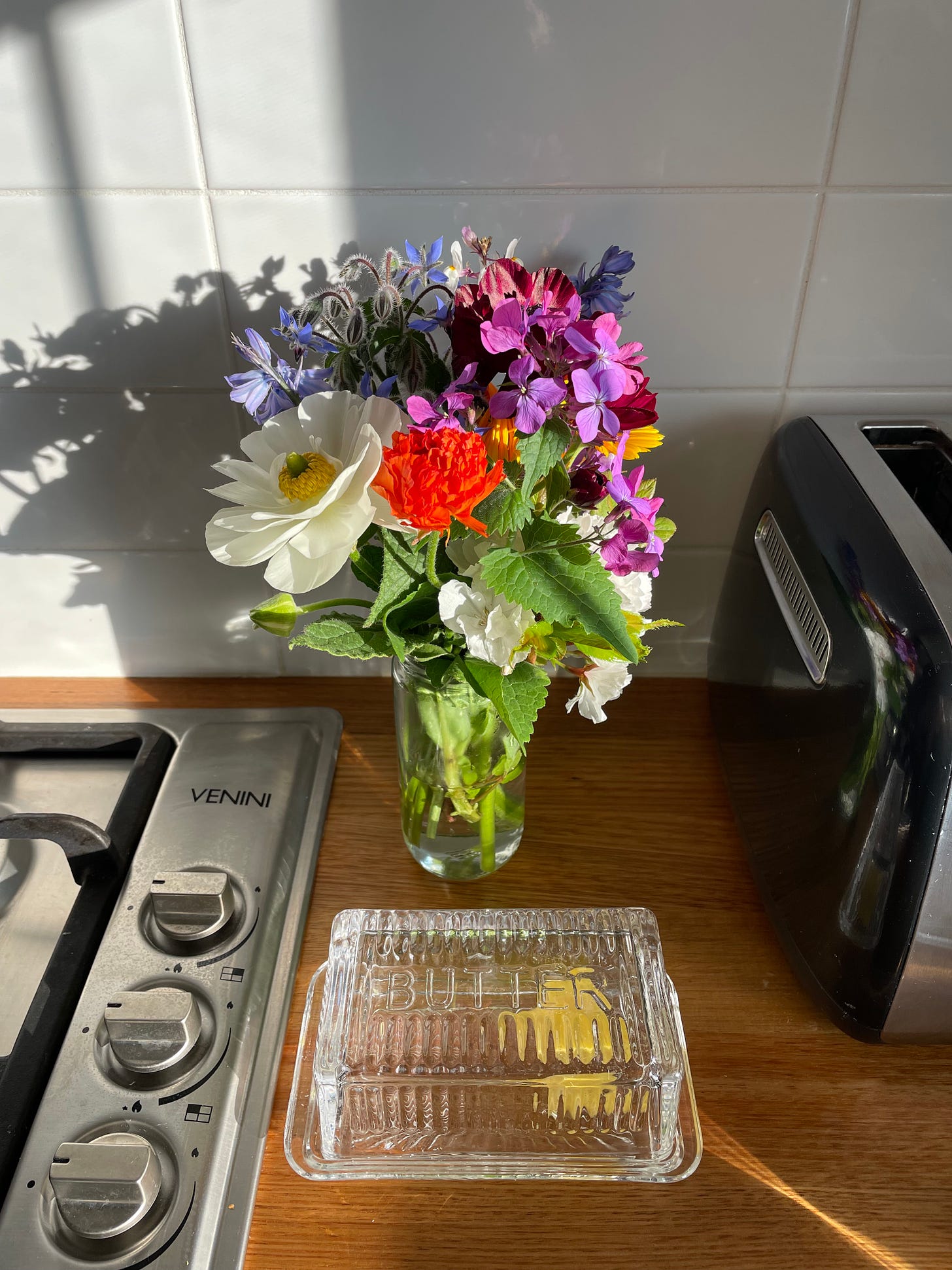 Colourful bouquet of flowers in a jar sitting on the kitchen counter next to a toaster and the stove.