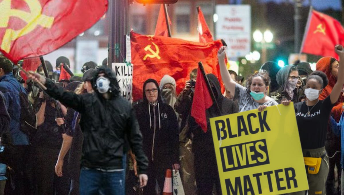 A group of antifa protesters gather, holding up BLACK LIVES MATTER and Communism flags.