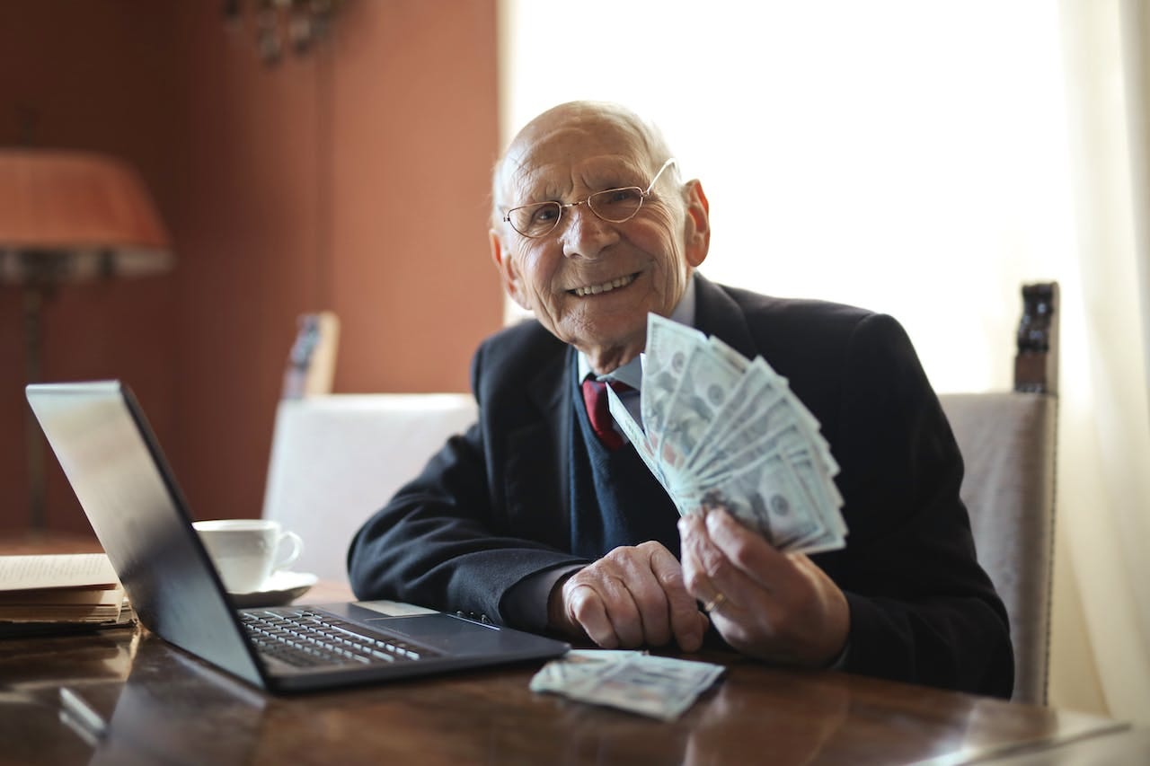 Senior businessman holding cash at his desk, with laptop