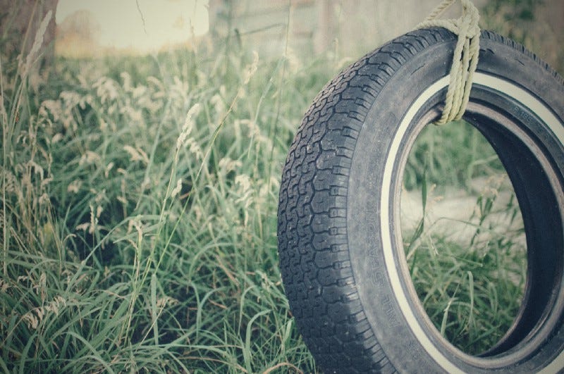 Rubber tire swing in overgrown yard.