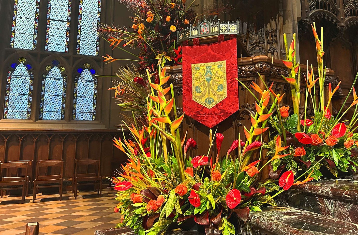 A display of red and orange flowers surrounding a pupit with a red and yellow cloth hanging.