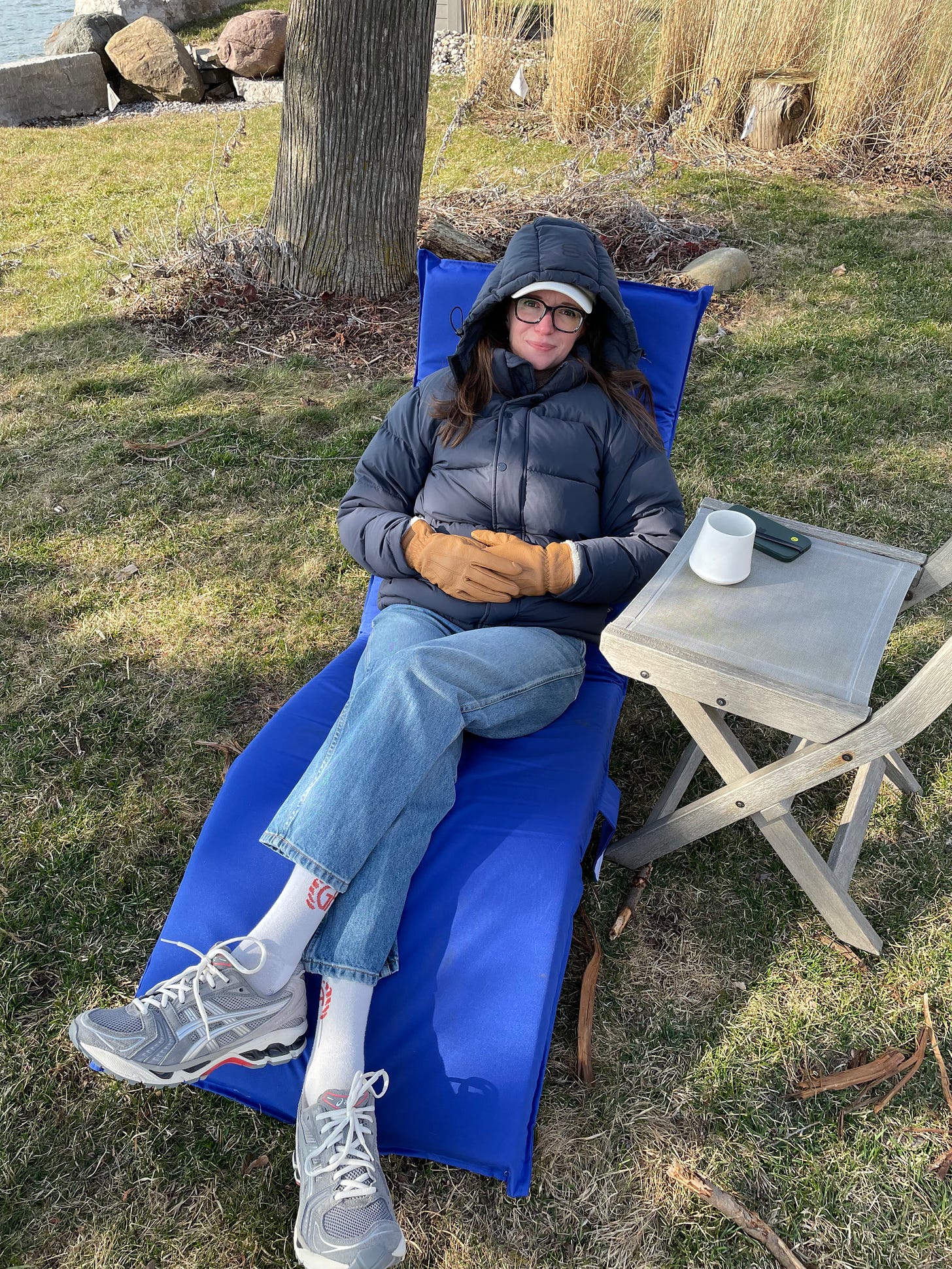 a white woman bundled up in a reclining chair smiles wryly