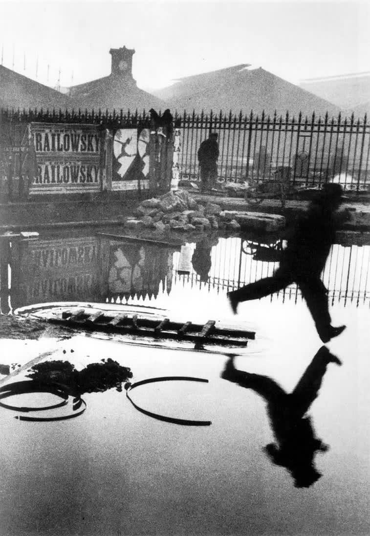 Black and white photo of a man leaping over a puddle