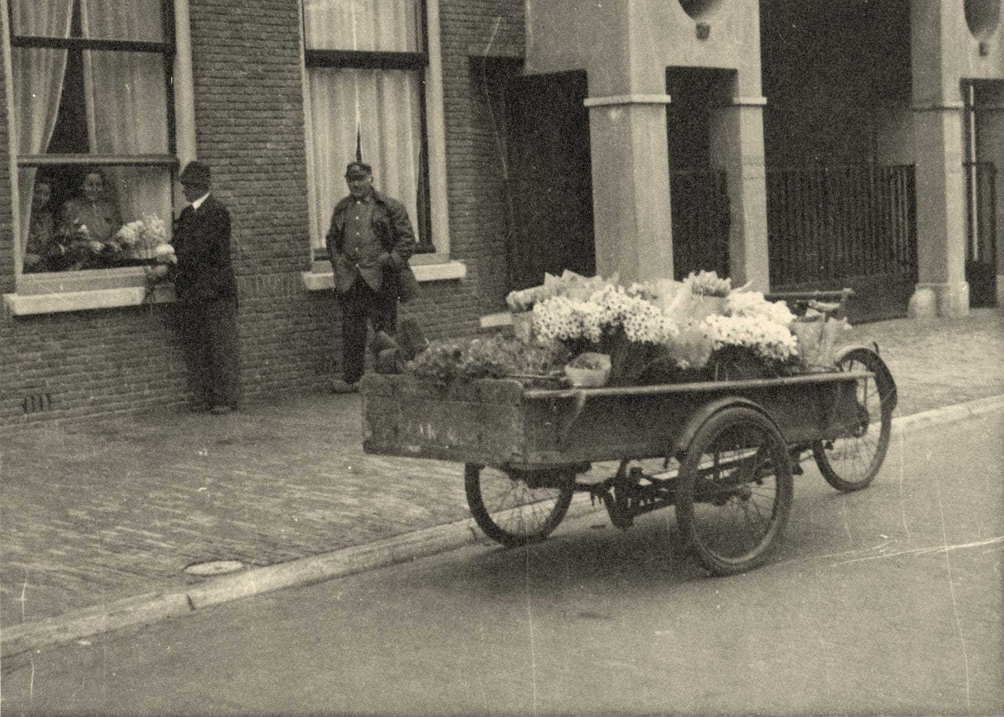 An old black and white photo showing a cargobike covered in flowers which are being sold.