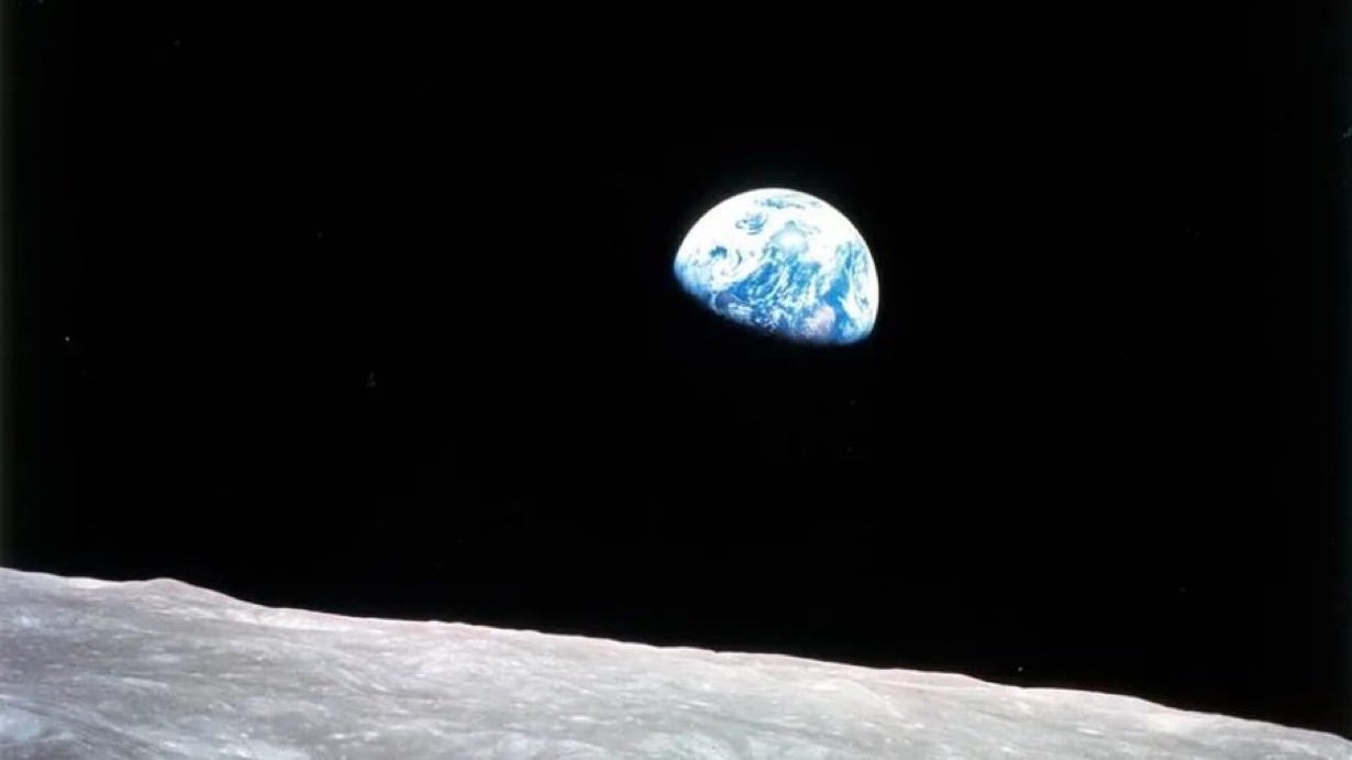 Bottom left: the surface of the moon. The rest of the photo is black except for in the top right, the blue-colored earth rising above the moon’s horizon.