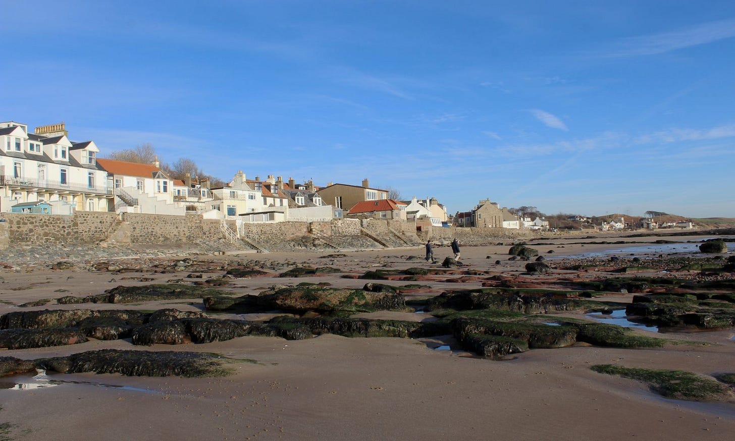 Lower Largo Beach in Fife, surrounded by apartments and homes. Two clothed beachgoers in the distant right side of the frame.