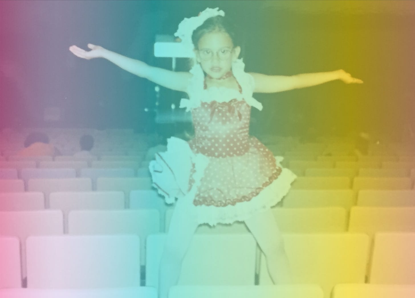 A rainbow-filtered photograph of little Shohreh in a red ballet costume with white polka dots throwing her hands up while standing on seats in an auditorium